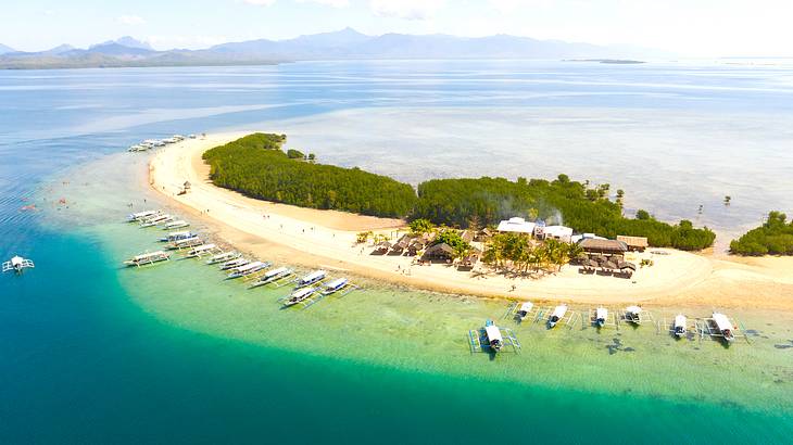 Aerial view of a sandy island with greenery surrounded by blue water and boats