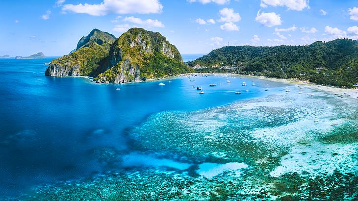 Aerial view of a beach with extensive reefs surrounded by hills covered with greenery