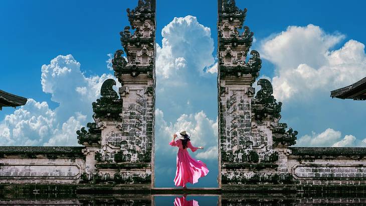 An ancient stone gate-like structure with a woman in a pink dress between the arch