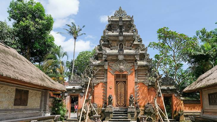 An orange temple structure with carvings next to a path and small huts