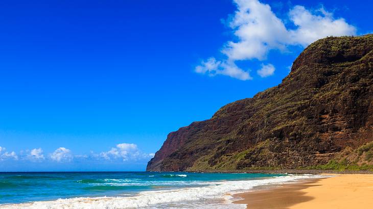 A cliff with a sandy beach and crystal blue ocean next to it under blue sky