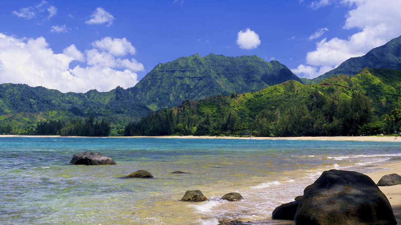 Ocean water flowing onto a beach with green mountains surrounding