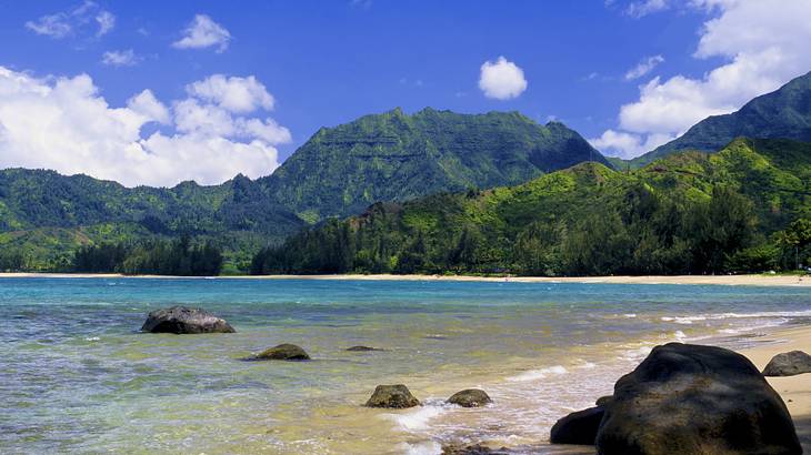 Ocean water flowing onto a beach with green mountains surrounding