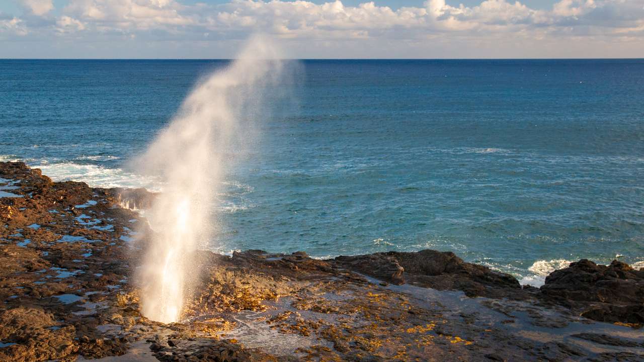 Volcanic rocks with water spouting out of them and the ocean behind