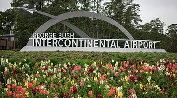 A sign "George Bush Intercontinental Airport" in a garden with multicolored flowers