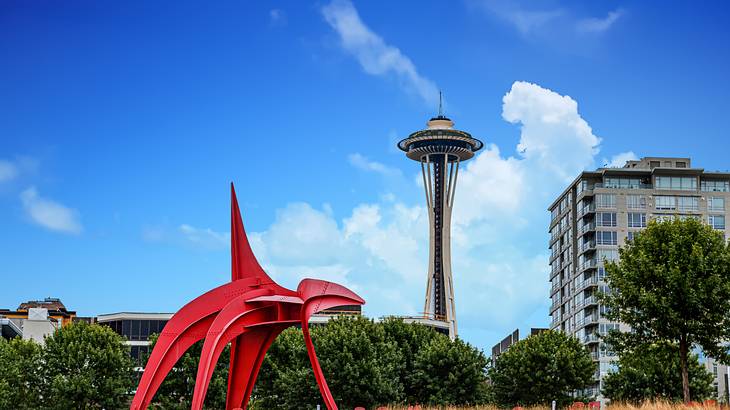 A red sculpture in a park with a building and observation tower behind it