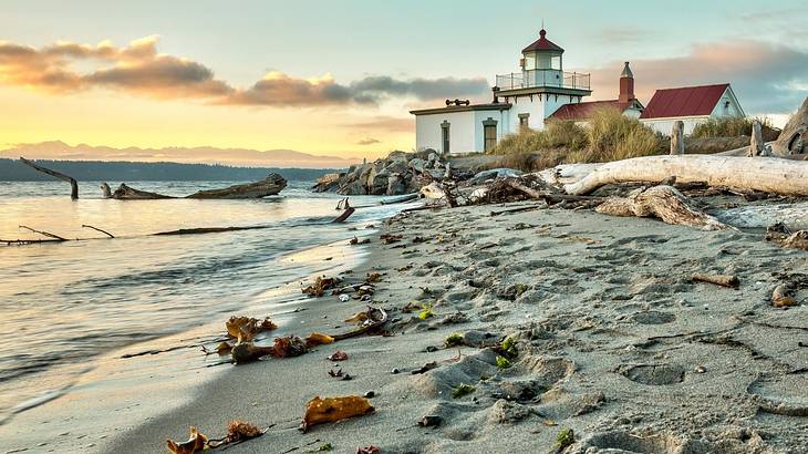A lighthouse building with a sandy shore and ocean around it at sunset