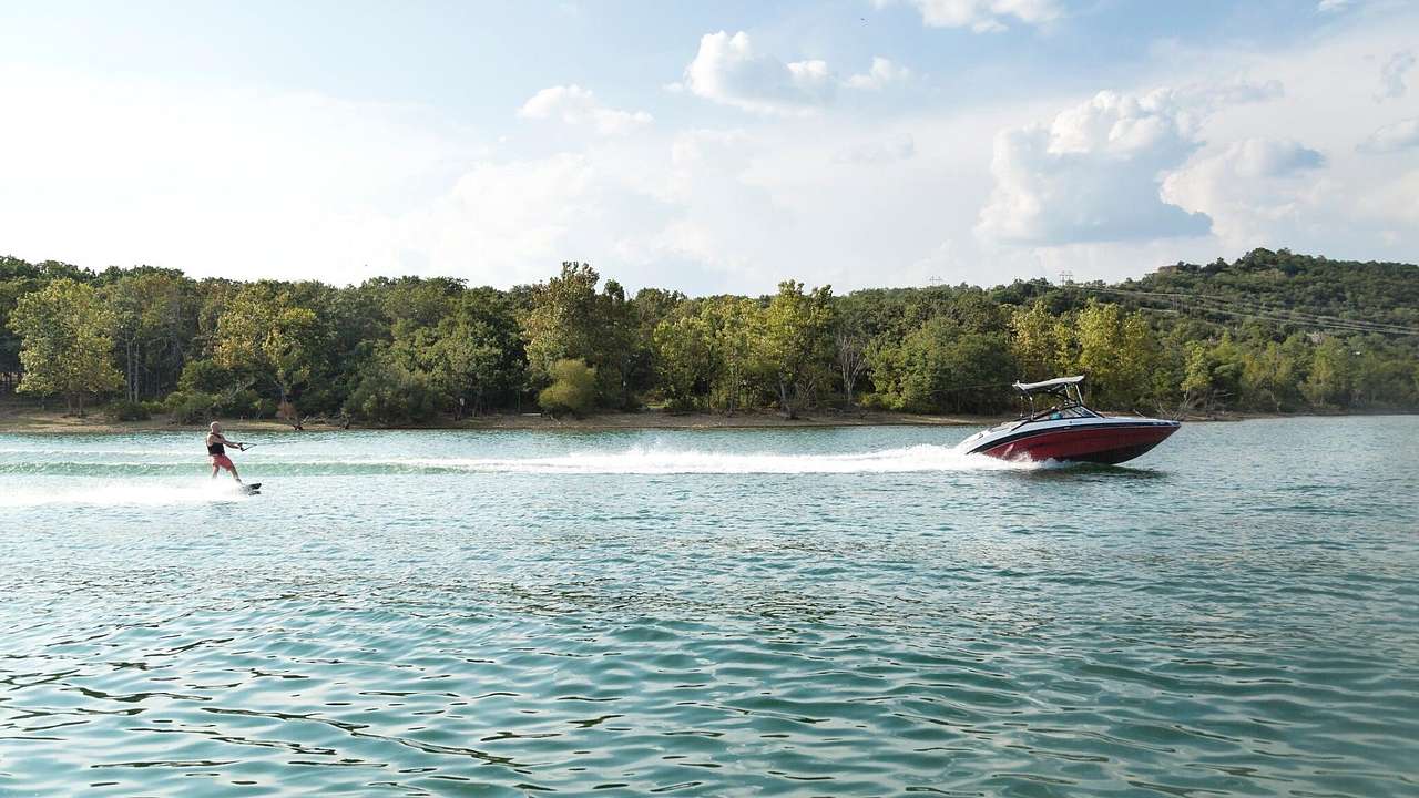 A lake with a boat and someone jet skiing and greenery-covered hills on the shore