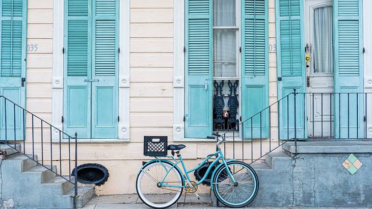 A blue bike in front of a house with a white exterior and blue shutters