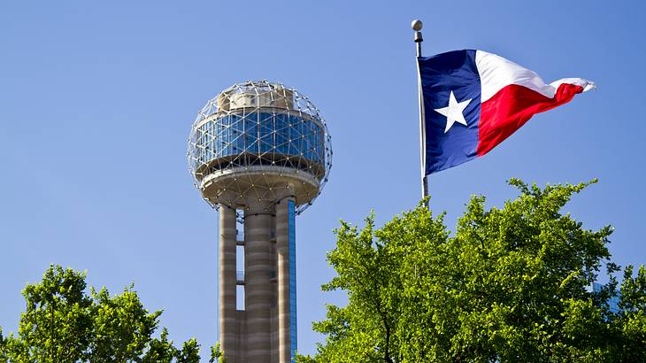 A tower with a round observation deck on the top and a Texas flag next to it