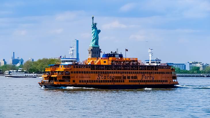 An orange passenger ferry on the water in front of the Statue of Liberty