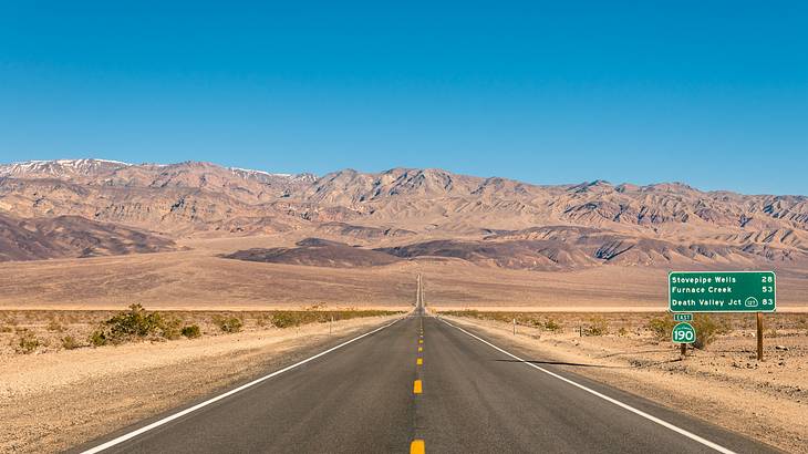 A road leading to sand-colored mountains with desert on either side