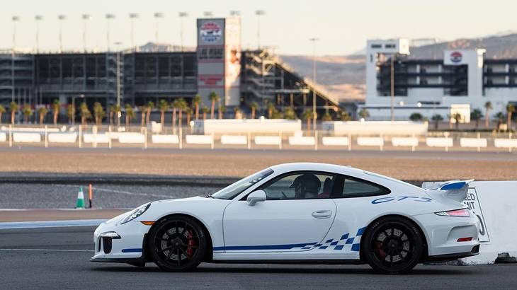 A white car on a race track with buildings in the background