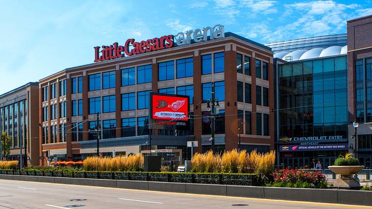 A building with many windows and a " Little Caesars Arena" sign next to a road A building with many windows and a " Little Caesars Arena" sign next to a road