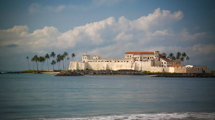 A castle fortress surrounded by water and tall palm trees