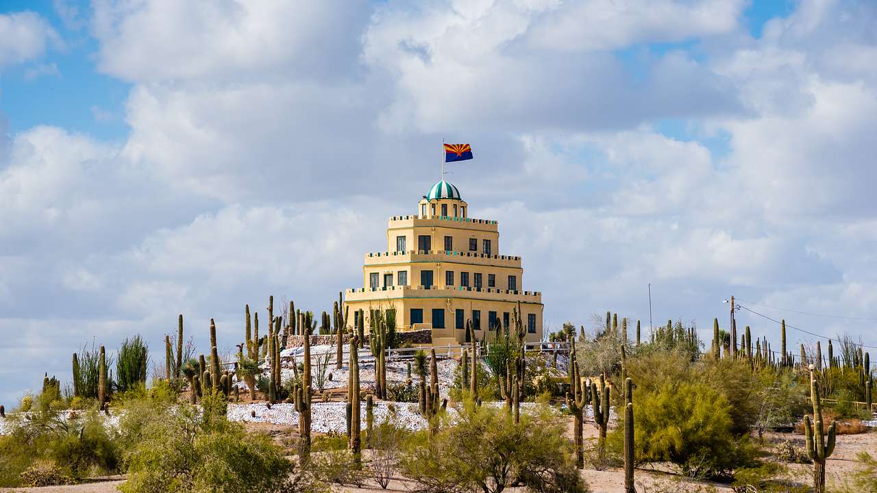 A large yellow castle in a desert surrounded by cacti