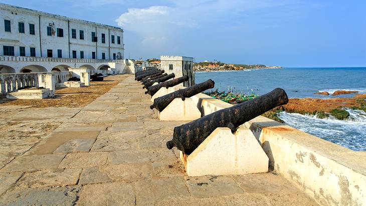 Cannons on a coastal concrete edge with a white rectangle building on the left