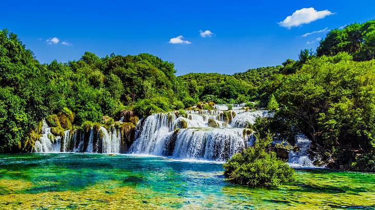 A waterfall flowing into a pool surrounded by green trees