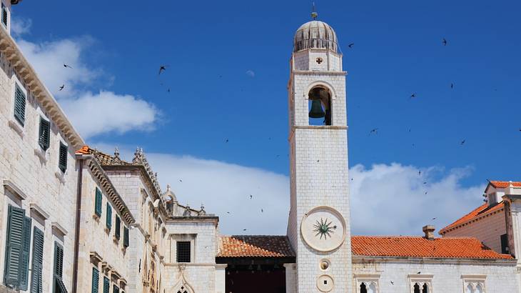 A clock tower next to stone houses on a clear day