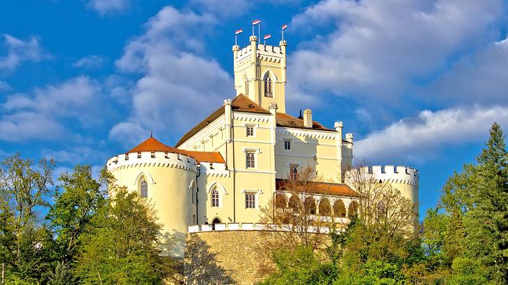 A large white castle with a tower and orange roofs next to trees