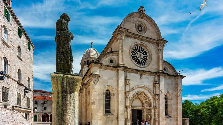 A large stone cathedral with an arched door next to a statue