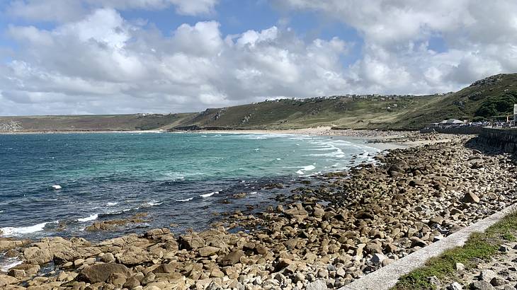Faraway view of blue water in a bay with green hills in the back and rocks in front