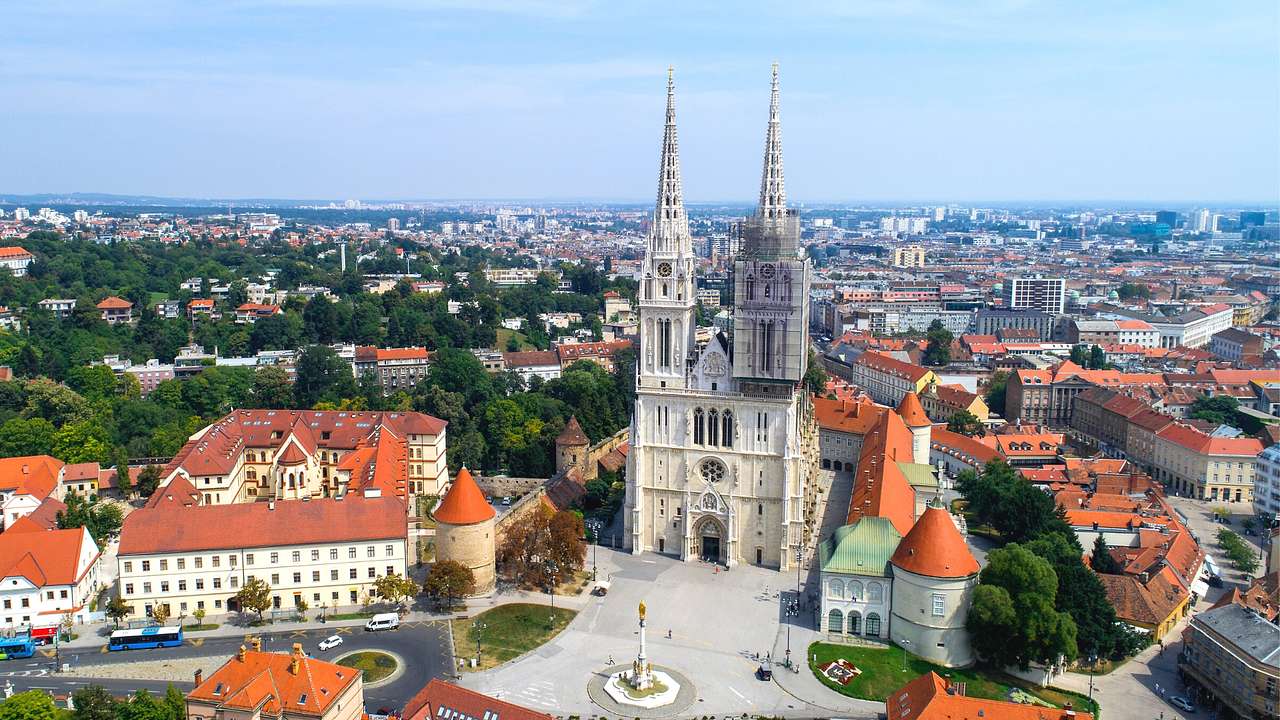 A cathedral with two towers in a square next to buildings with orange roofs