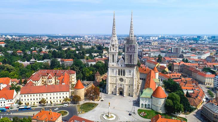 A cathedral with two towers in a square next to buildings with orange roofs