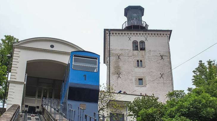 A blue incline train next to a tower and green trees