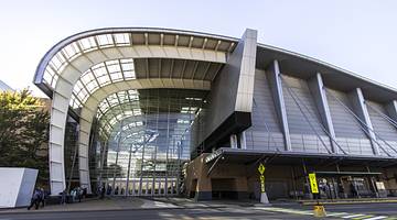 A modern building with glass and an arch next to a road and trees
