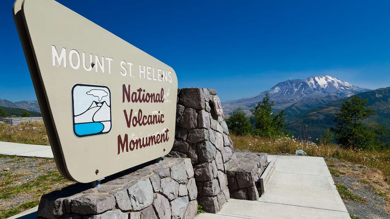 A sign saying Mount St Helens National Volcanic Monument with a volcano at the back