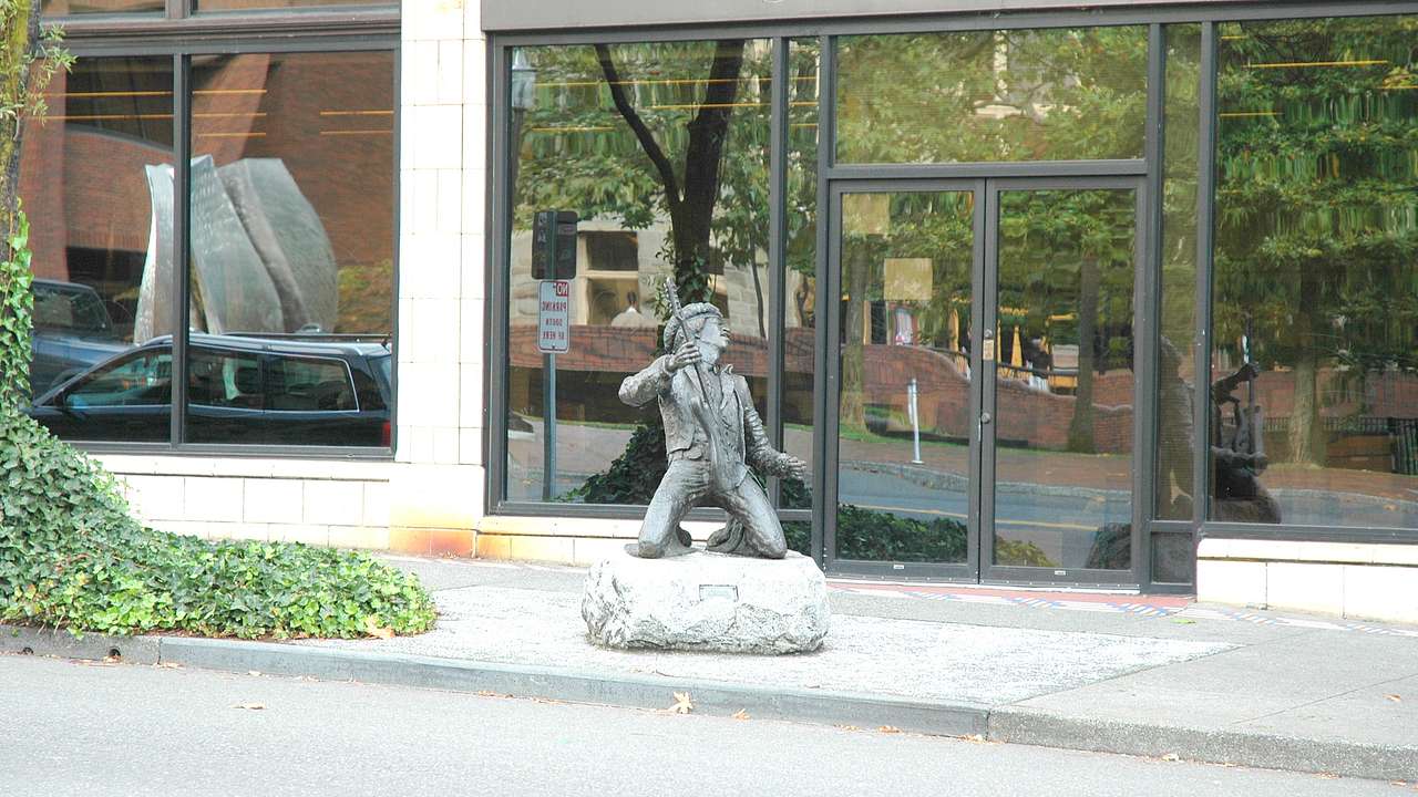 A statue of a man kneeling and holding a guitar in front of a building