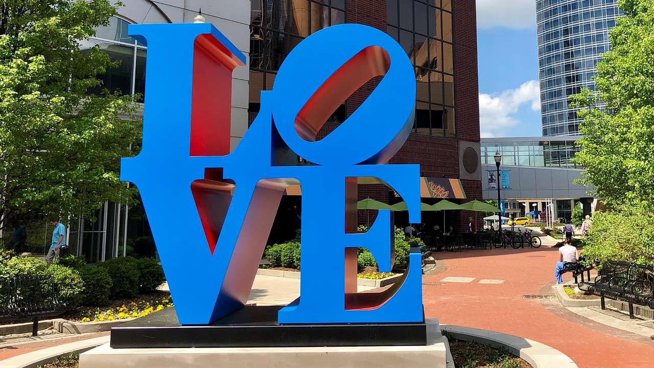A blue sculpture of the word "Love" in a square with trees and a red brick path