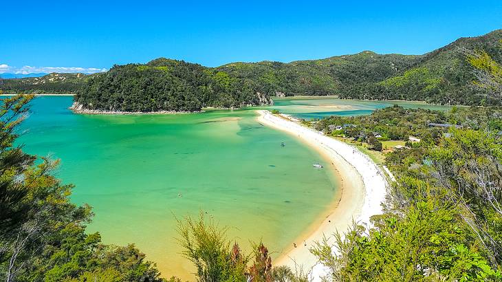 Aerial view of a white sand coastline with small tree-filled hills and blue water