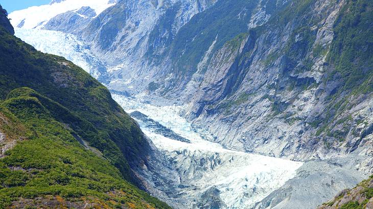 A glacier in between mountains going down into a body of water