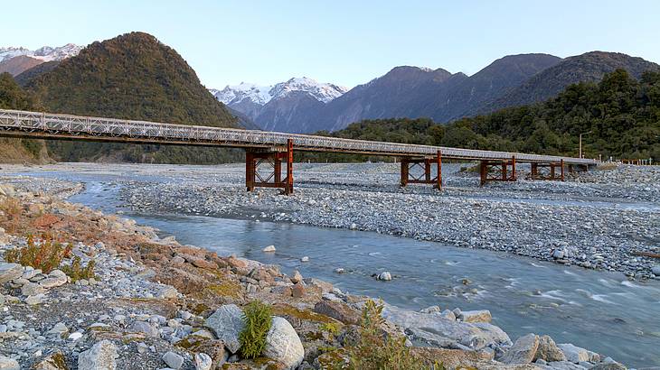 A bridge over a river broken up over rocks with mountains at the back