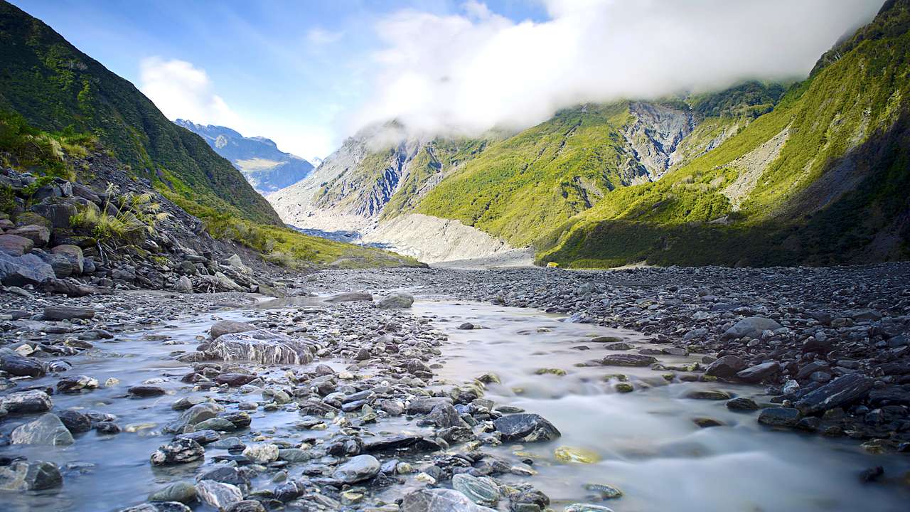 A water flowing from a glacier between mountains with rocks and water in front