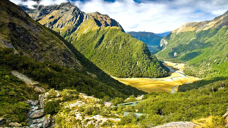 Aerial view of a stream in between majestic mountains under partially cloudy skies