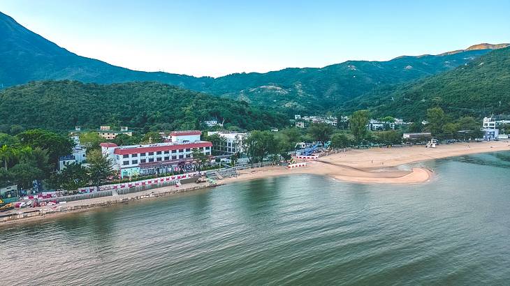 A beach with a group of buildings and lush mountains behind, Mui Wo, Hong Kong