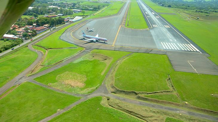 An airplane on a tarmac surrounded by green fields with mountains in the background