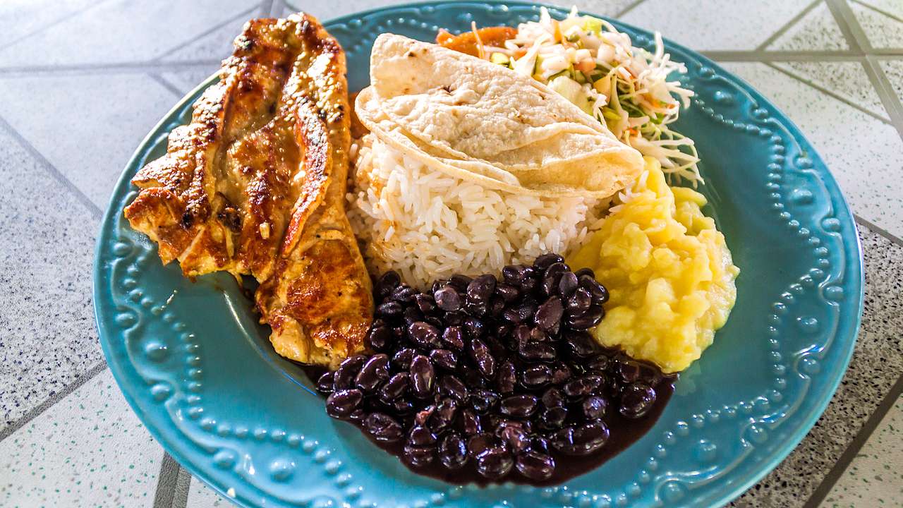 Grilled meat, black beans, white rice, and vegetables served on a blue plate