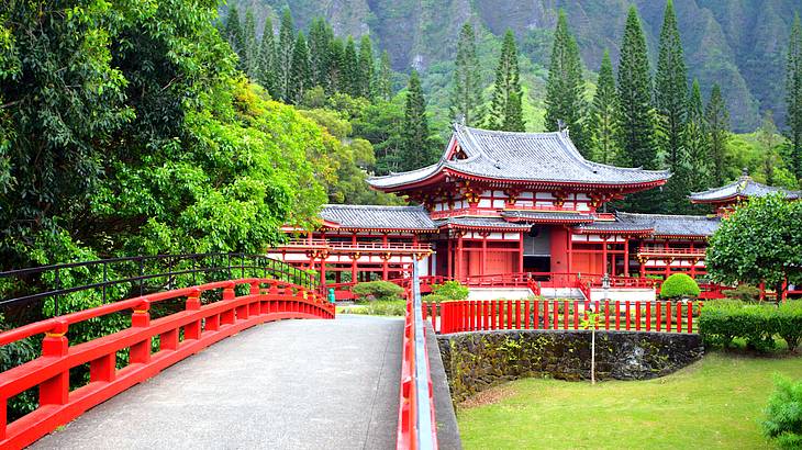 A red Buddhist temple facing a bridge with a backdrop of trees and a mountain
