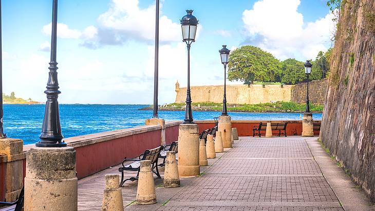 Antique street lamp and benches on a promenade facing the water and cliffs with trees