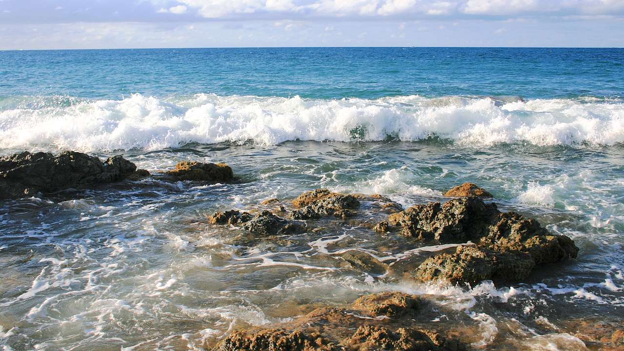 A beach with waves crashing on big rocks on a sunny day
