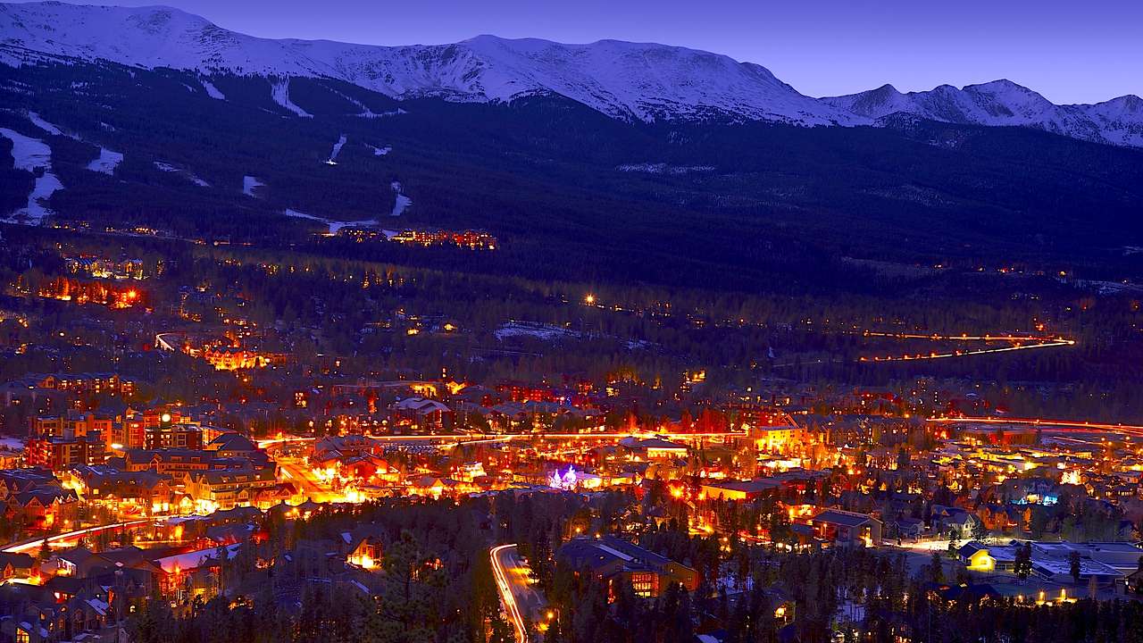 Aerial of homes lit up at night with dark snow-capped mountains in the back