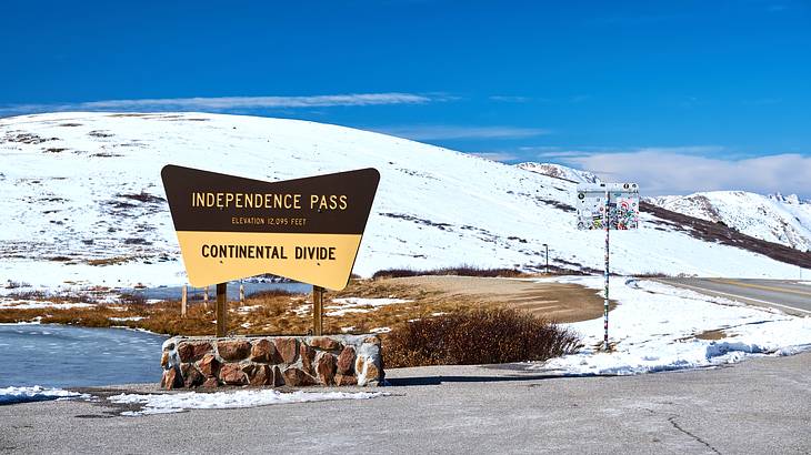 The Independence Pass signage with snow-covered hills and a body of water at the back