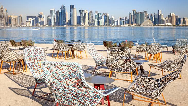 A skyline full of tall buildings with water and chairs and tables in front