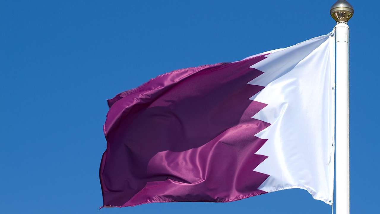 A white and maroon colored flag on a pole, fluttering under a blue sky