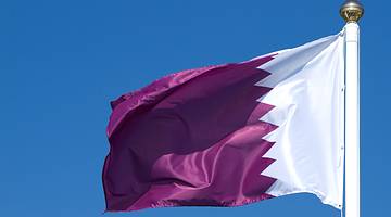 A white and maroon colored flag on a pole, fluttering under a blue sky