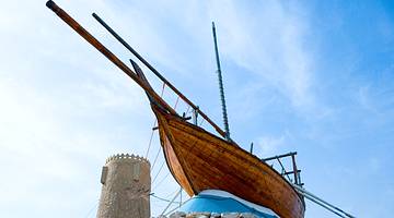 A stone fort in the background of a wooden boat perched on a pedestal of rocks